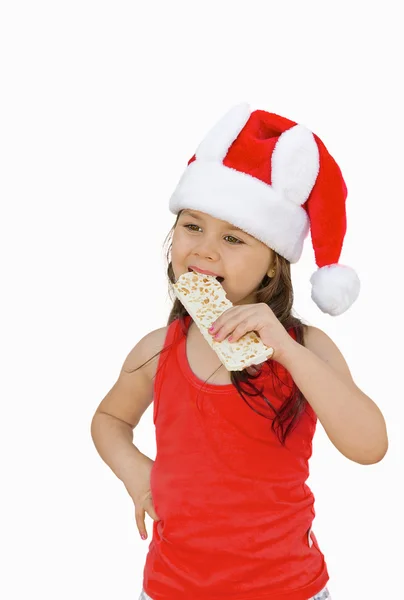 Little girl wearing red Santa hat eating white chocolate with pe — Stock Photo, Image