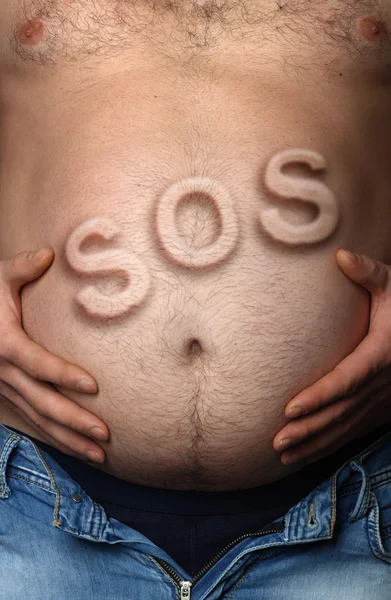 Man's maag met inscriptie Sos uitsteekt — Stockfoto