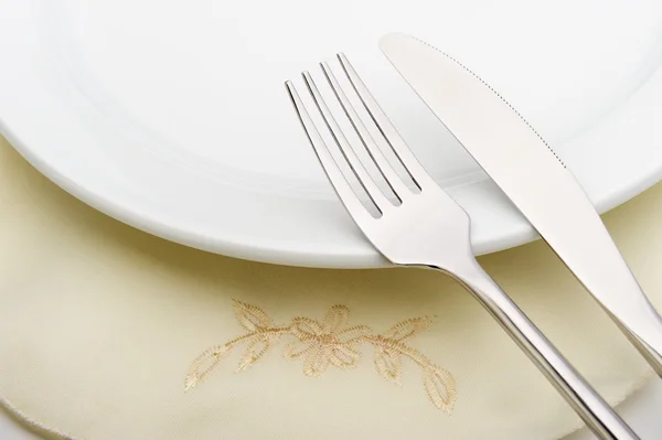 Fork and a knife lie on serviette and a plate — Stock Photo, Image