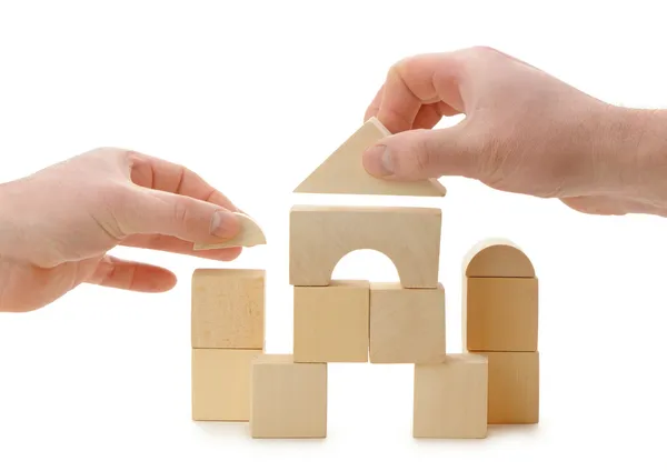 Die Hände bauen ein Spielzeugdach auf Holzwürfeln auf — Stockfoto