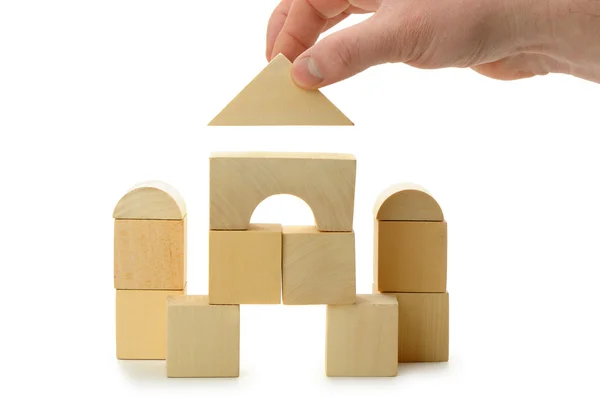 La mano stabilisce un tetto giocattolo su cubi di legno — Foto Stock