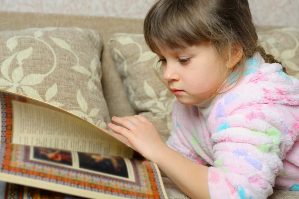 Девочка читает книгу, лежащую на диване — стоковое фото