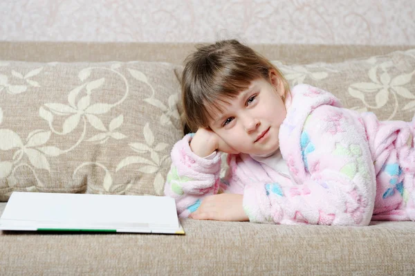 La niña lee el libro acostada en un sofá — Foto de Stock