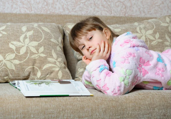 Маленька дівчинка читає книгу, що лежить на дивані — стокове фото