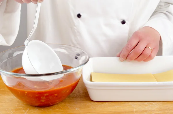 Ženské kuchař s rajčatovou omáčkou, přípravu lasagne — Stock fotografie