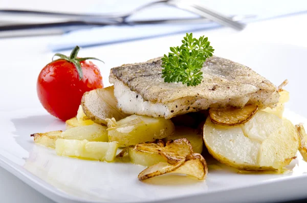 Filetto di eglefino su un piatto con patate grigliate e aglio — Foto Stock