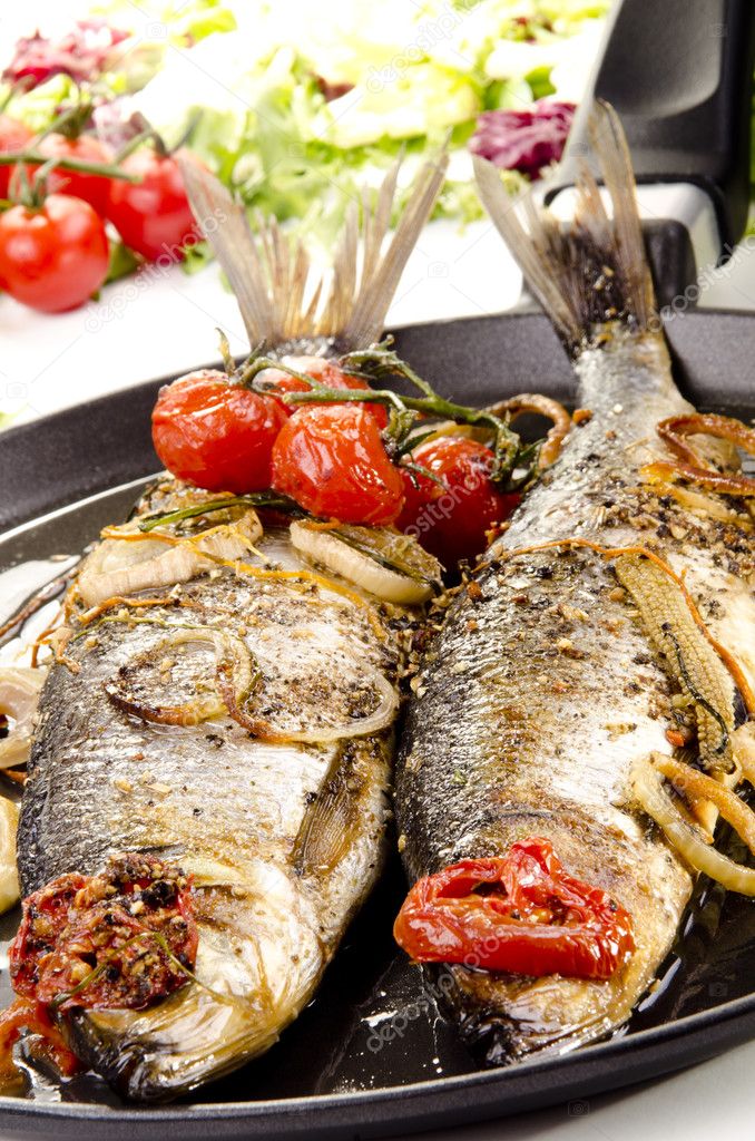 Two grilled sea bass in a pan with tomato and onion