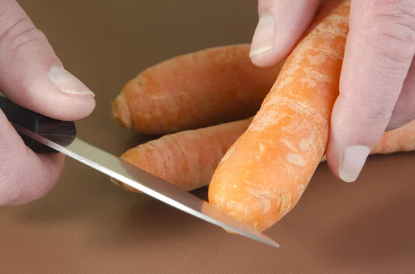 Female chef cuts a carrot with a kitchen knife — Stock Photo, Image