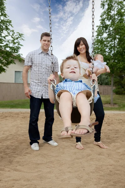 Père et mère poussant garçon sur balançoire — Photo