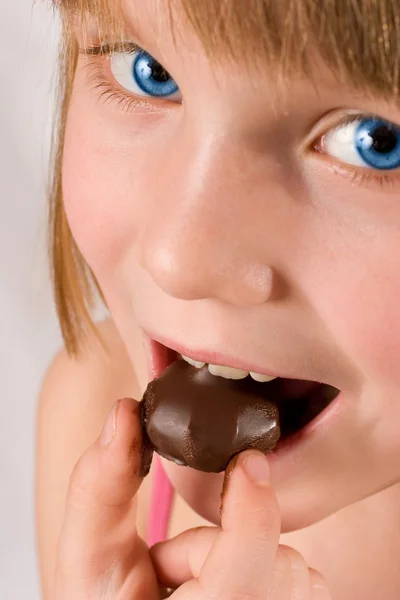 Vacker liten flicka med blå ögon äta choklad godis isol — Stockfoto