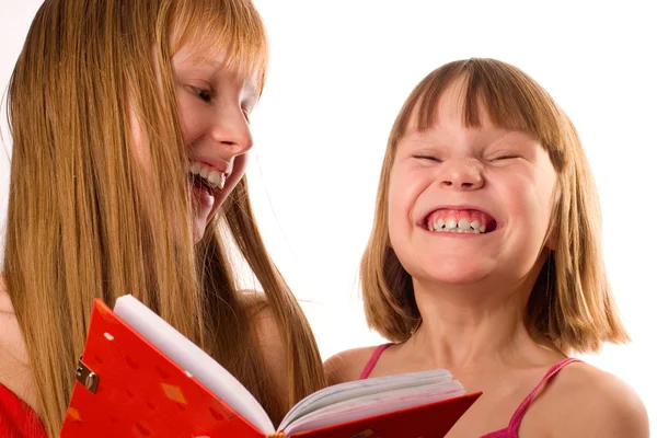 Zwei kleine Mädchen, die wie Schwestern aussehen, ein rotes Buch in der Hand und lachen — Stockfoto
