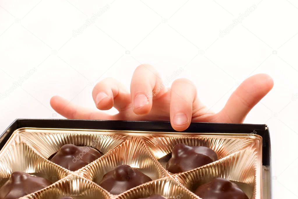 Child's hand picking chocolate candy from box isolated over whit