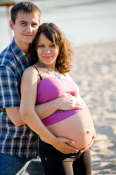 Беременная женщина с мужем на пляже — стоковое фото