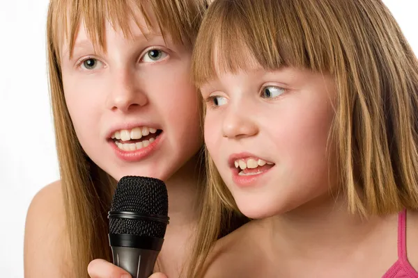 Две младшие сестры поют в микрофоне — стоковое фото