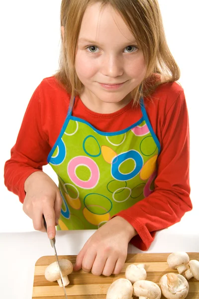 Little girl wearing apron slicing mushrooms — ストック写真