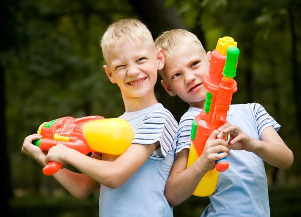 Dois irmãos gêmeos sorridentes com pistolas de água — Fotografia de Stock