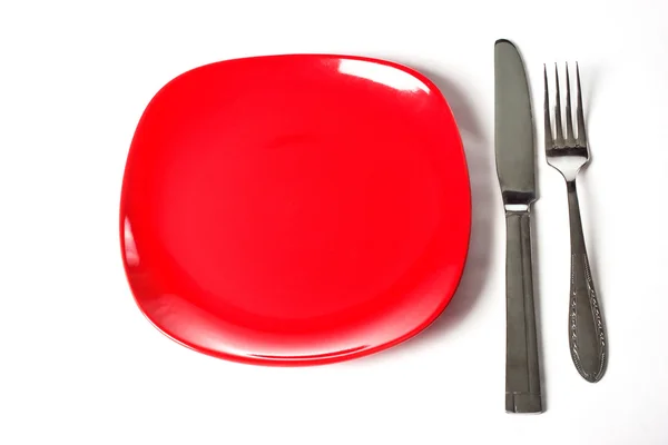 Красная тарелка, нож и вилка изолированы на белом — стоковое фото