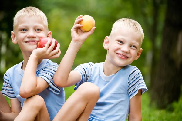 Dos hermanos gemelos sonrientes sosteniendo frutas — Foto de Stock