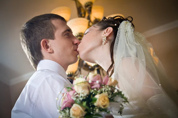 Красивая молодая невеста целует жениха в помещении — стоковое фото