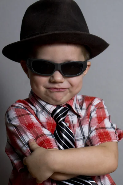 Мальчик в шляпе и черных очках на сером фоне — стоковое фото