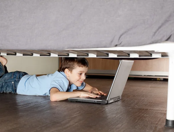 Niño jugando portátil debajo de la cama — Foto de Stock