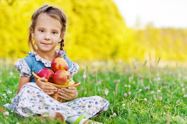 Little girl sitting on grass with basket of apples clipart