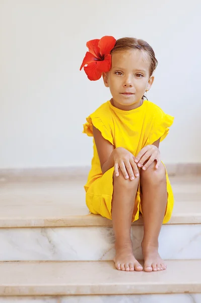 Liten flicka i gul klänning med röd blomma — Stockfoto