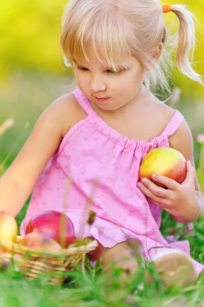 Ξανθό κοριτσάκι που κάθεται στο γρασίδι με μήλα — Φωτογραφία Αρχείου