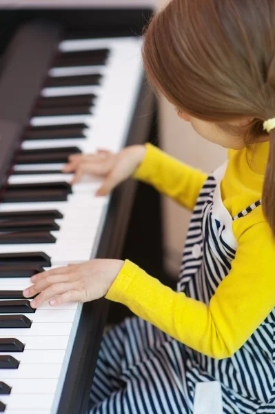 Liten flicka i gul klänning spelar piano — Stockfoto