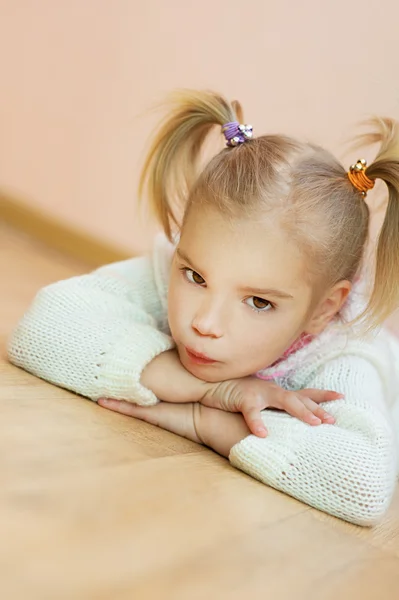 Маленька дівчинка в білому светрі лежить на підлозі — стокове фото