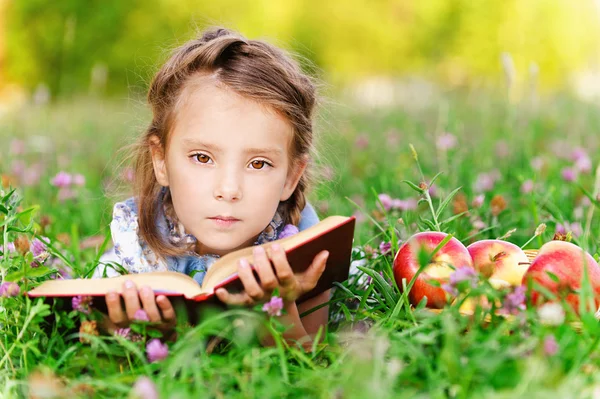 小女孩躺在草地上苹果与书 免版税图库图片