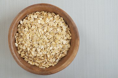 Rolled oats in a wooden bowl on a gray cloth. clipart