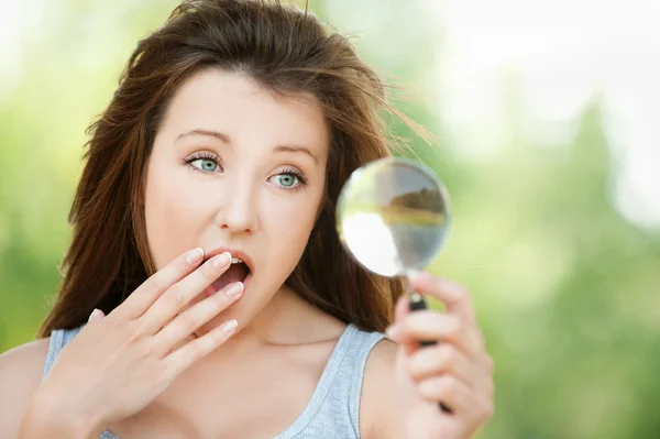 Amazed young woman looks through magnifier — Stock Photo, Image