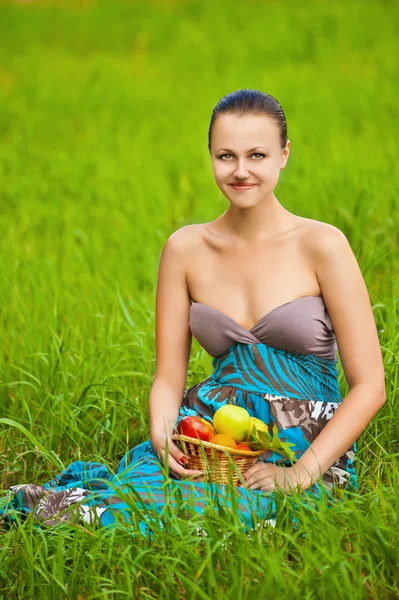 Femme tenant un panier de fruits assis sur l'herbe — Photo