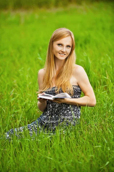 Jovem mulher senta-se na grama e livro de leitura — Fotografia de Stock