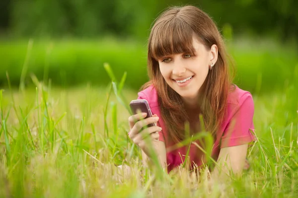 Молодая женщина с мобильным телефоном лежит на зеленой траве — стоковое фото