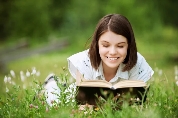 Jonge vrouw ligt op gras en boek leest — Stockfoto