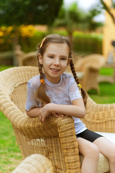 Little girl sits in wicker chair — Stock Photo, Image