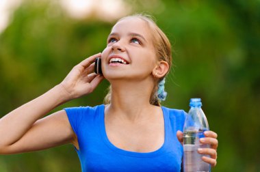Smiling teenager girl with bottle talking on phone