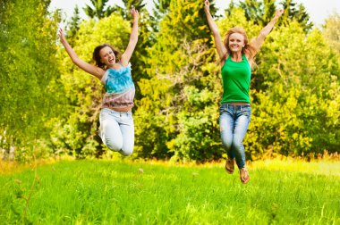 Two young beautiful girls jumps up at summer green park clipart