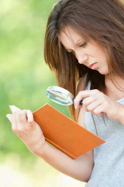 Молодая женщина увеличитель рассматривает книгу — стоковое фото
