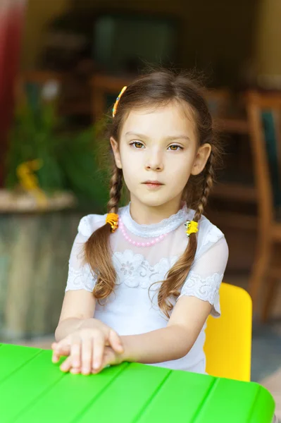 Küçük kız yeşil masada oturuyor — Stok fotoğraf