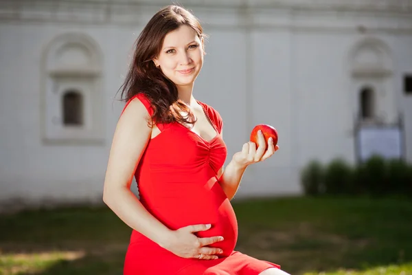 Беременная женщина сидит на улице с красным яблоком — стоковое фото