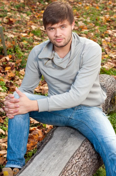 На відкритому повітрі портрет щасливого молодого чоловіка, що сидить в осінньому парку — стокове фото