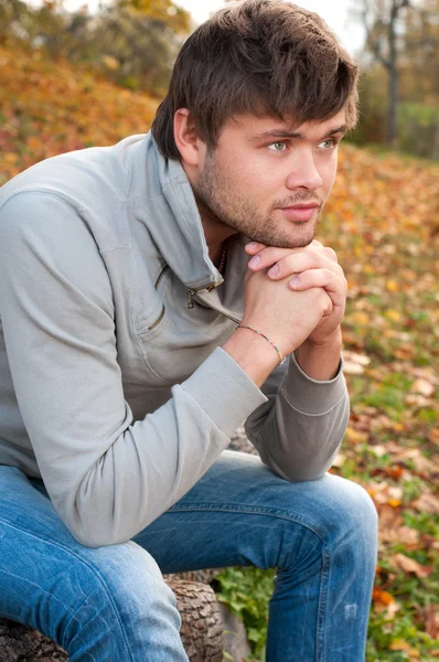 Na zewnątrz portret szczęśliwy młody człowiek siedzi w parku jesień — Zdjęcie stockowe
