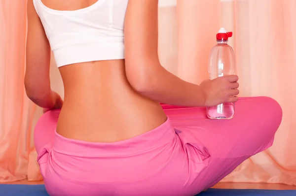 Junge Frau sitzt auf einer Yogamatte und hält eine Flasche Wasser in der Hand — Stockfoto