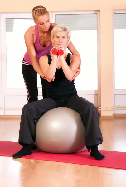 Trainer helping woman in doing exercise on ball — Stock Photo, Image