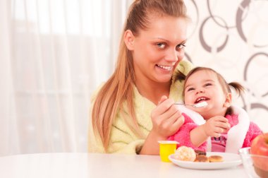 Portrait of young woman feeding her baby clipart