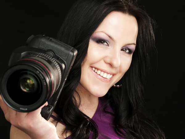 Smiling photographer woman holding camera over dark — Stock Photo, Image