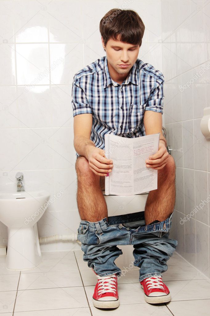 Man sitting on toilet and reading magazine.